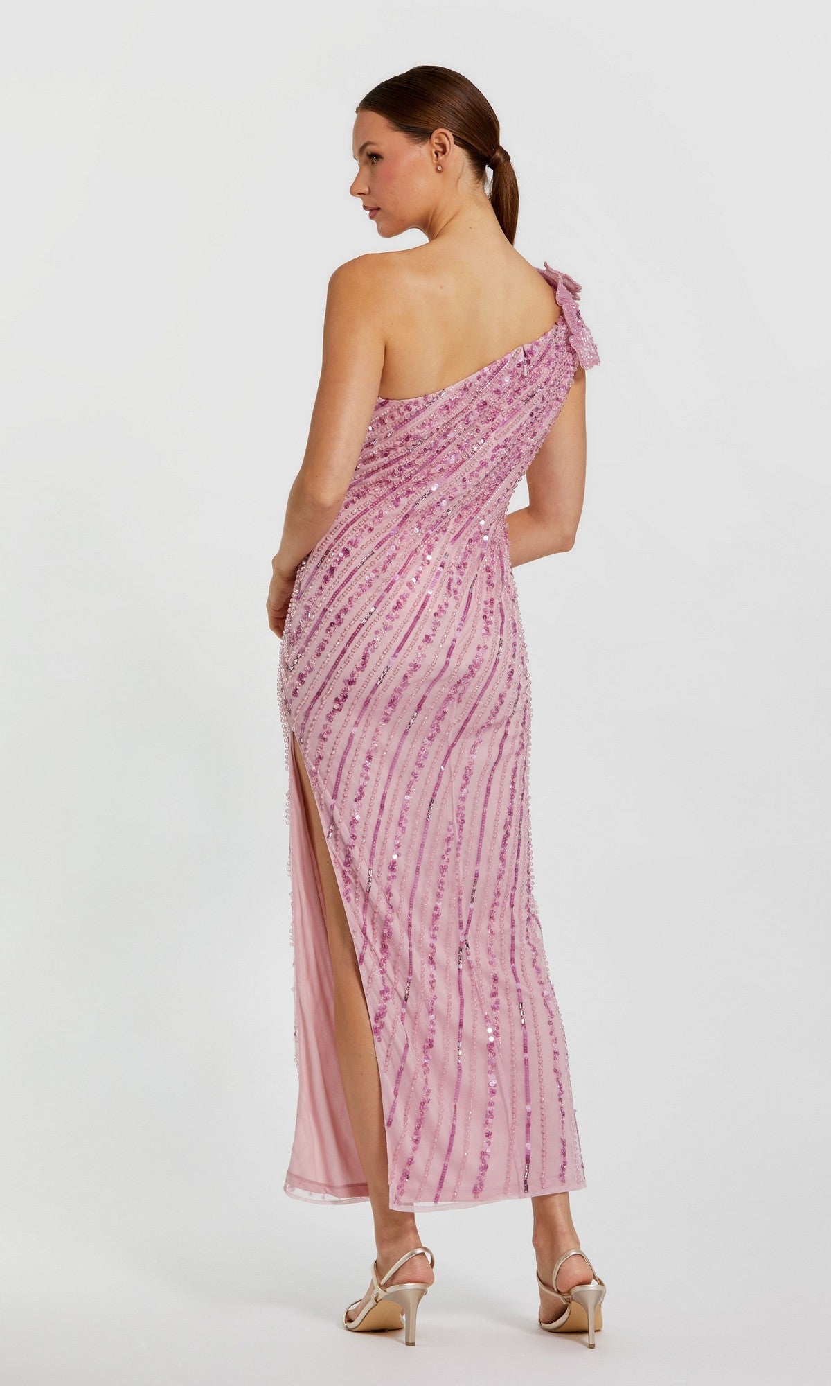 Woman wearing the Mac Duggal 94221 long formal dress in pink, featuring sequins, a one shoulder design, and side slit, stands in profile against a plain white background.